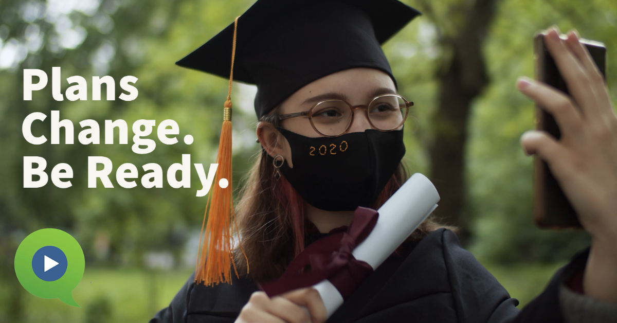 Young graduate holding diploma and phone while wearing a cloth face mask.