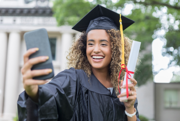 Graduate holding degree and phone for selfie.