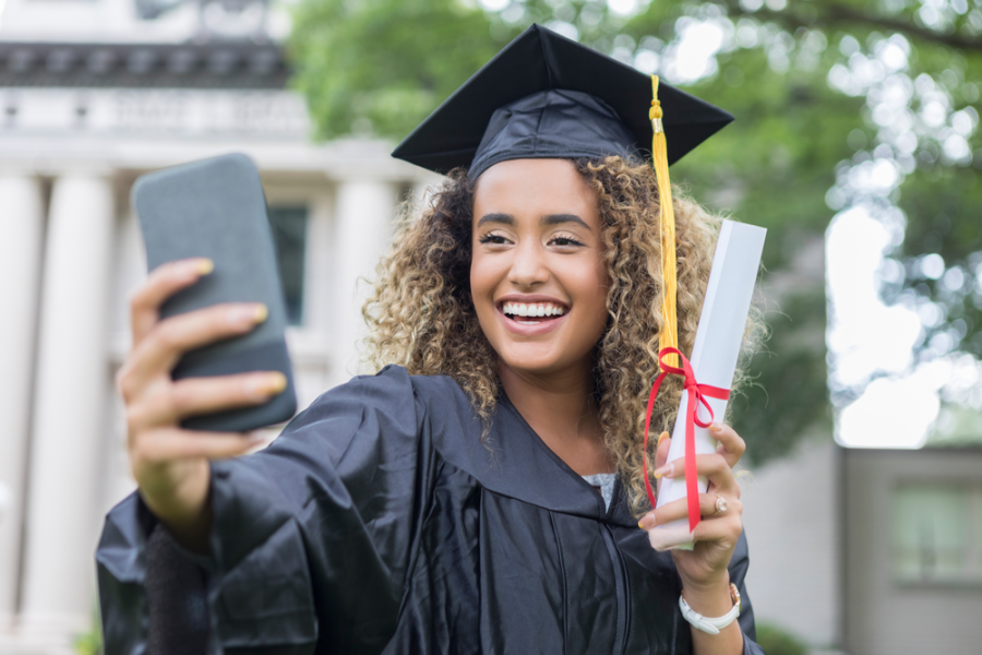 Graduate holding degree and phone for selfie.